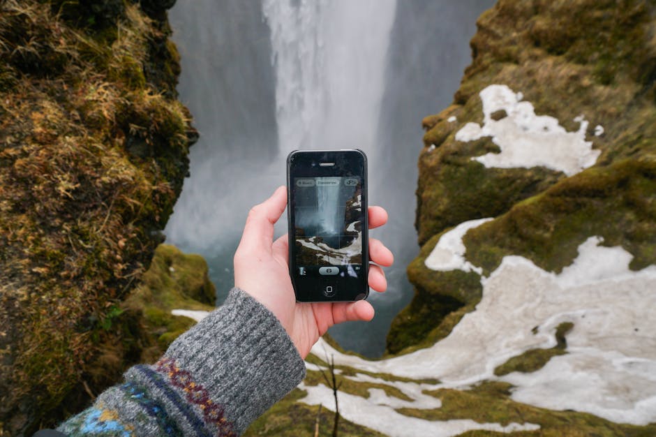 Mano fotografiando una cascada con el smartphone entre rocas cubiertas de musgo
