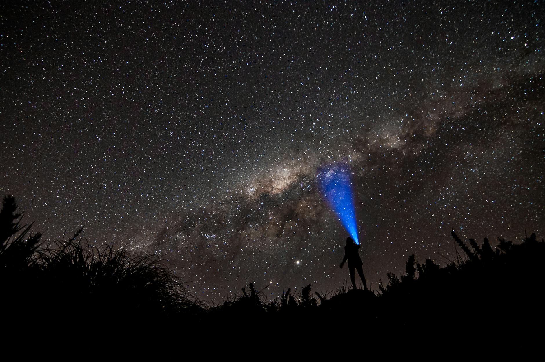 Persona observando la Vía Láctea con linterna bajo cielo estrellado