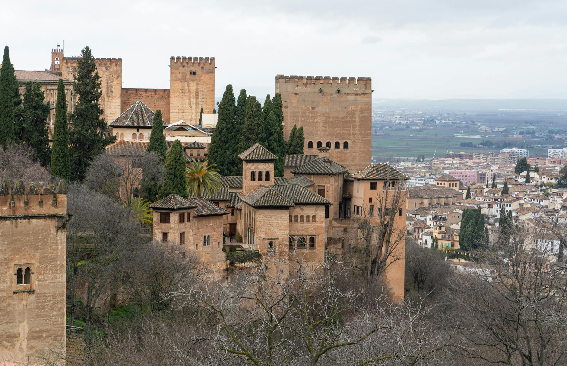 Vista escenica de la Alhambra rodeada de arboles con la ciudad de Granada al fondo