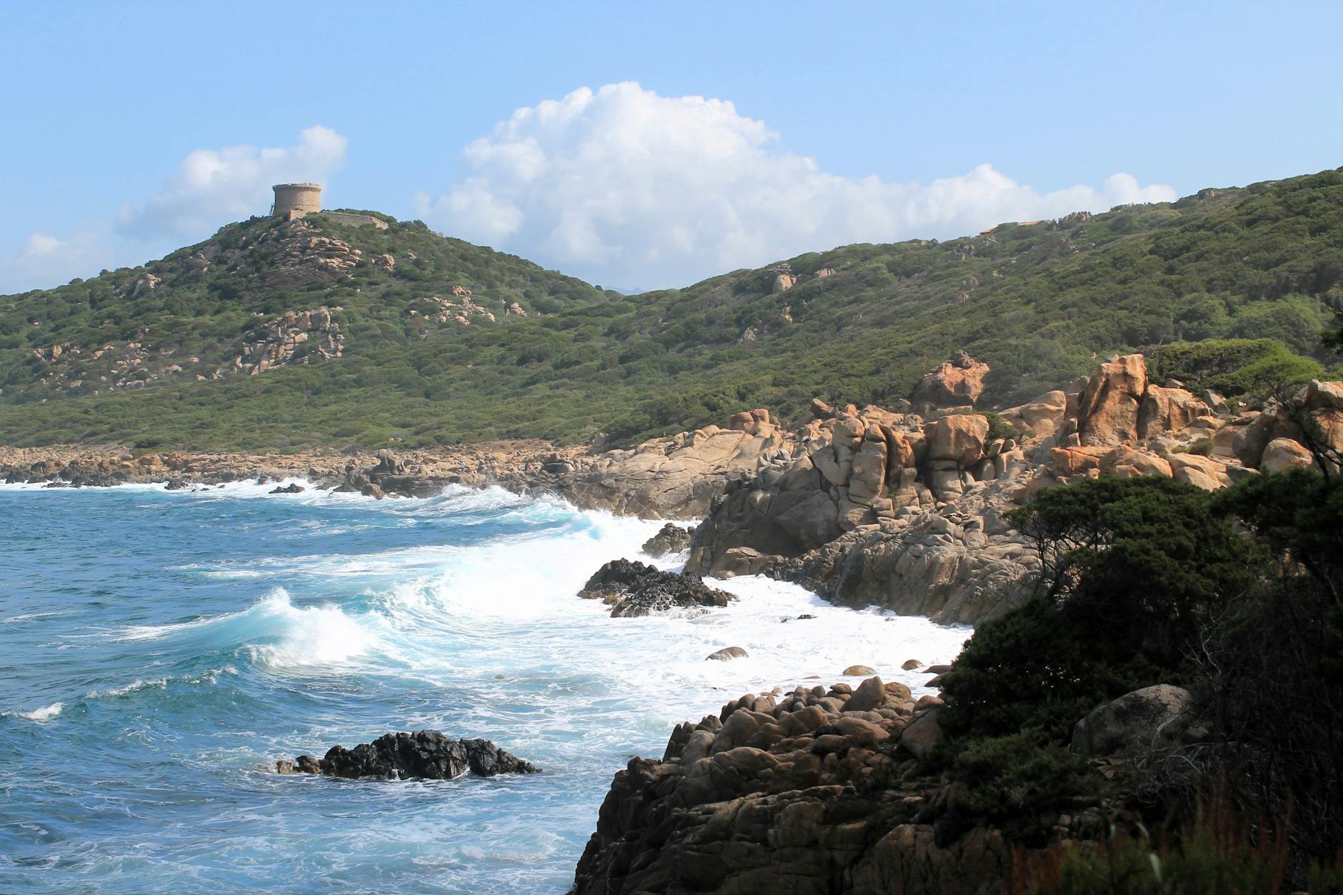Costa salvaje de Cerdeña con torre histórica en lo alto y olas rompiendo