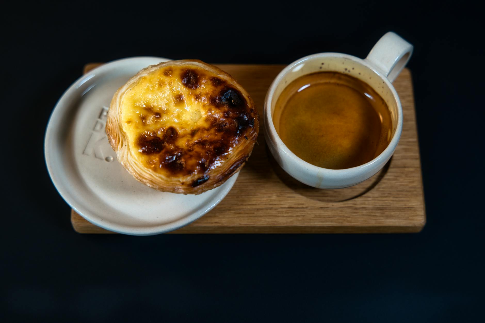 Pastel de nata portugues con espuma de canela junto a una taza de cafe espresso