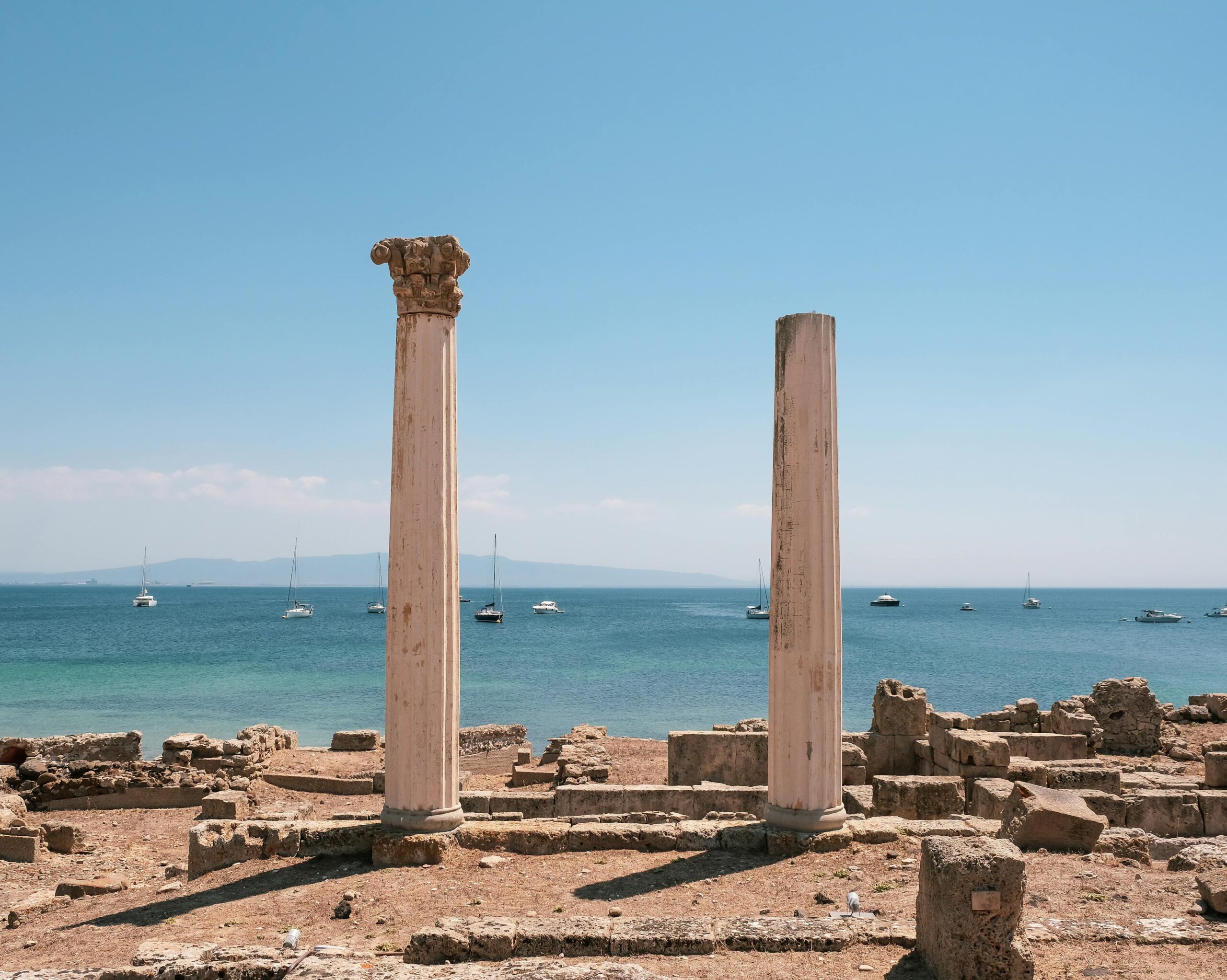 Columnas romanas del yacimiento de Nora en la costa de Cerdeña con yates al fondo