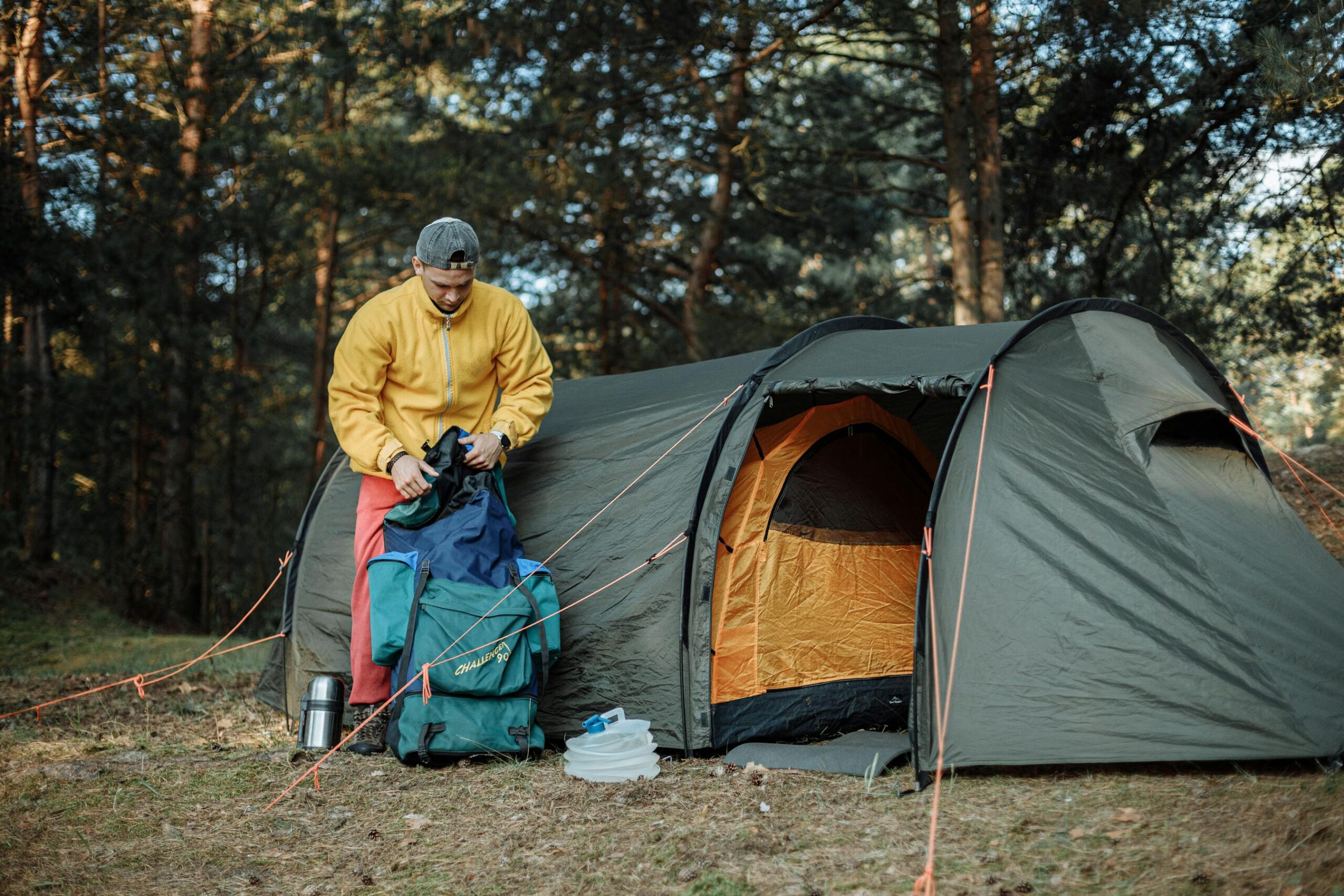 Joven organizando equipo de acampada junto a una tienda en el bosque