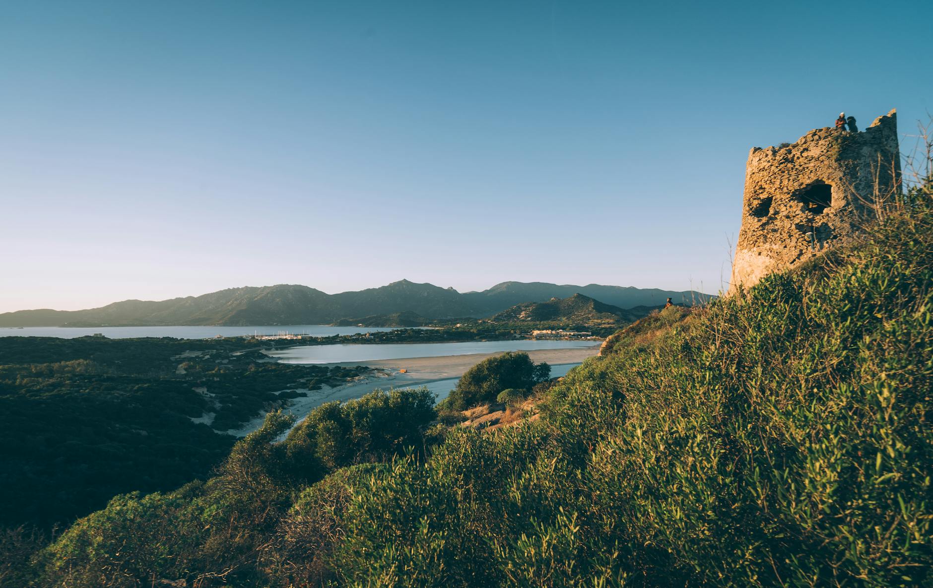 Bahía costera de Cerdeña con montañas y torre antigua al atardecer