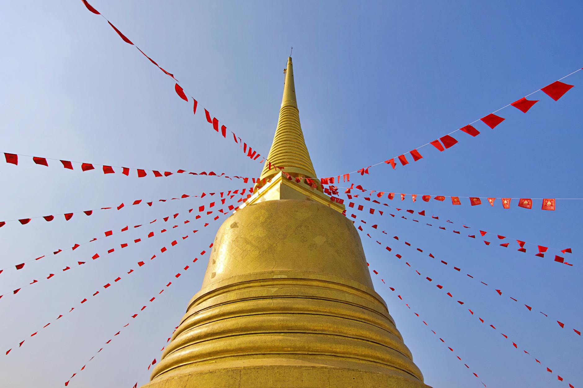 Chedi dorado con banderas rojas en Bangkok, Tailandia, bajo un cielo azul despejado