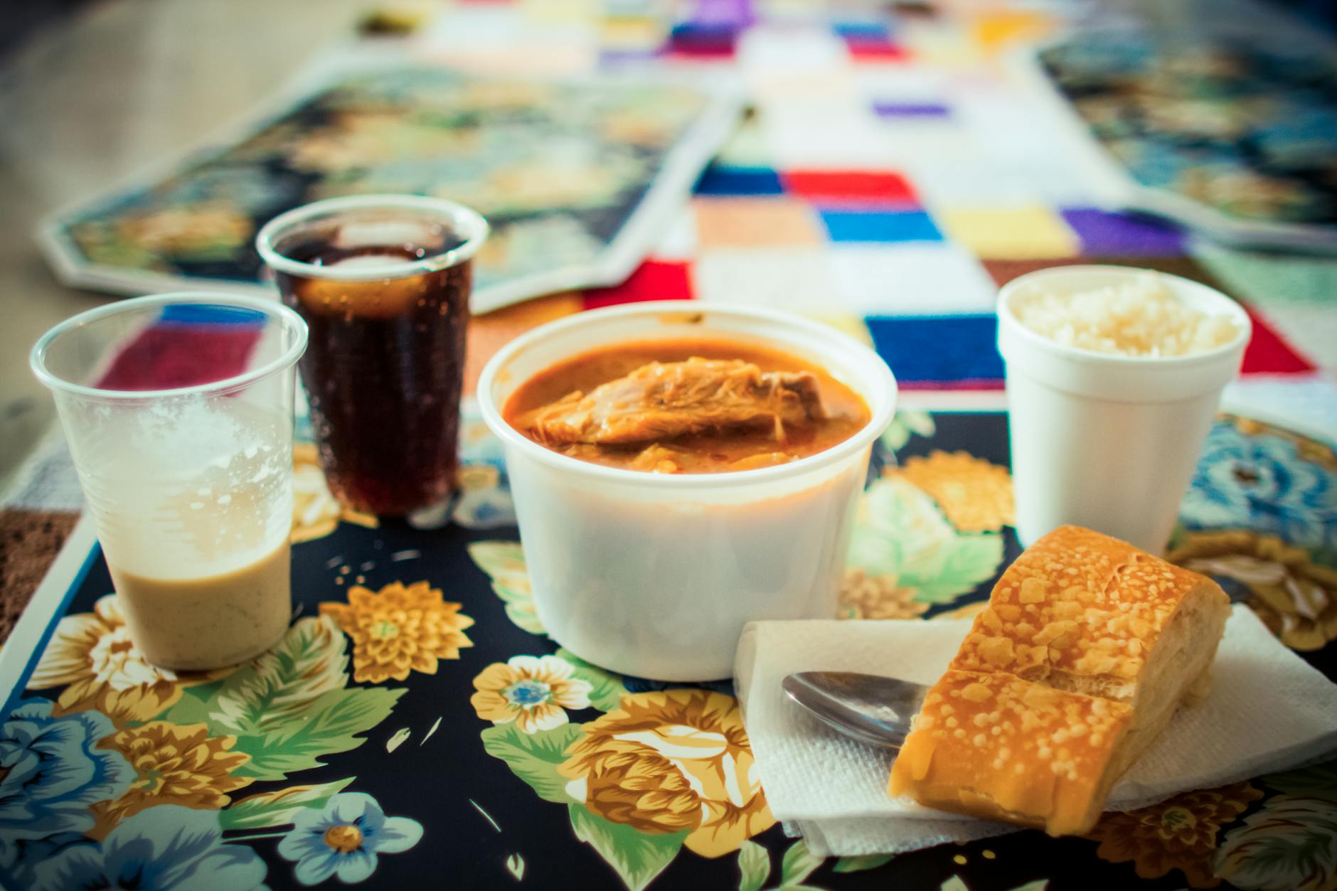 Mesa cubana con arroz, sopa, pan y bebidas sobre mantel estampado