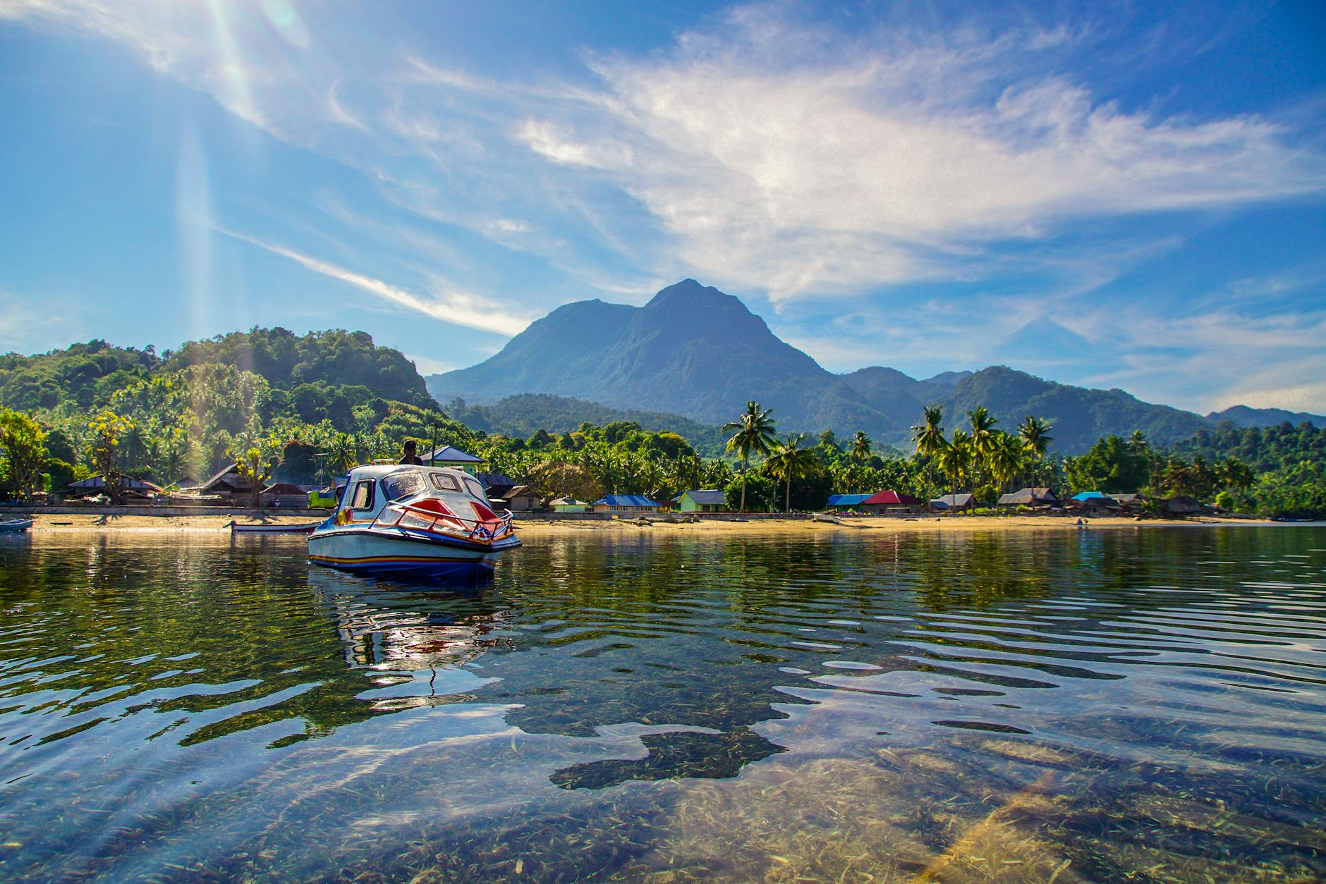 Playa tropical virgen en las Islas Molucas con aguas cristalinas y montañas al fondo