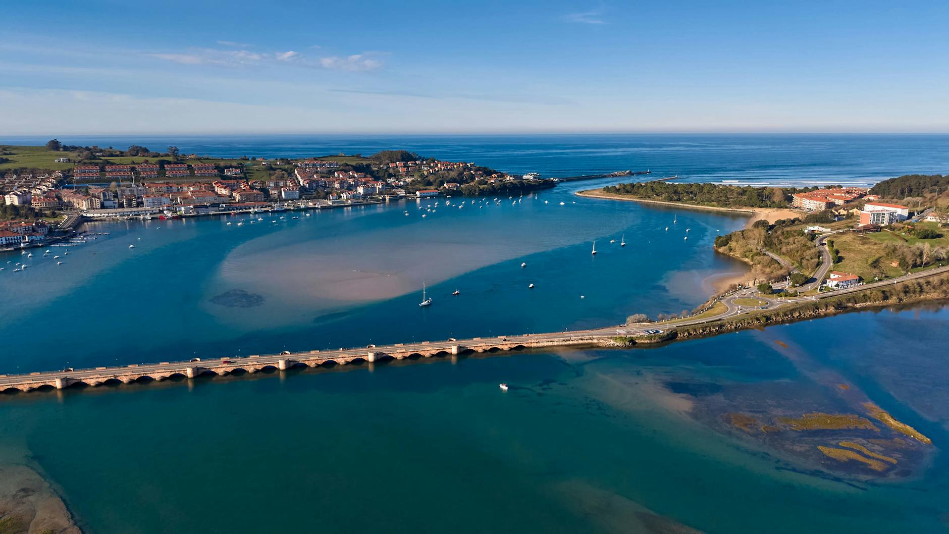 Vista aérea de la costa de Cantabria con puente y pueblo marinero al fondo
