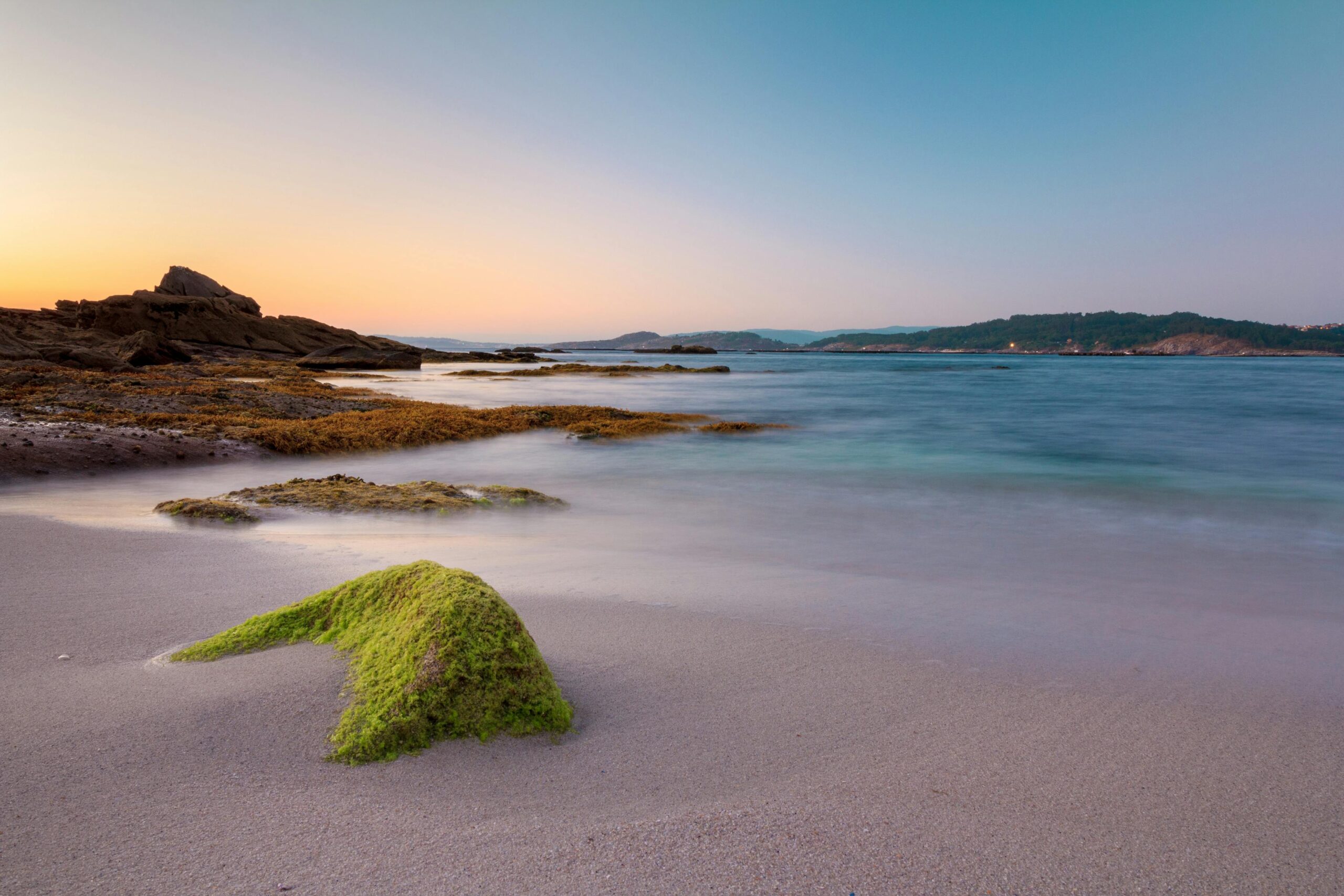 Amanecer sobre playa rocosa de Galicia con rocas cubiertas de musgo