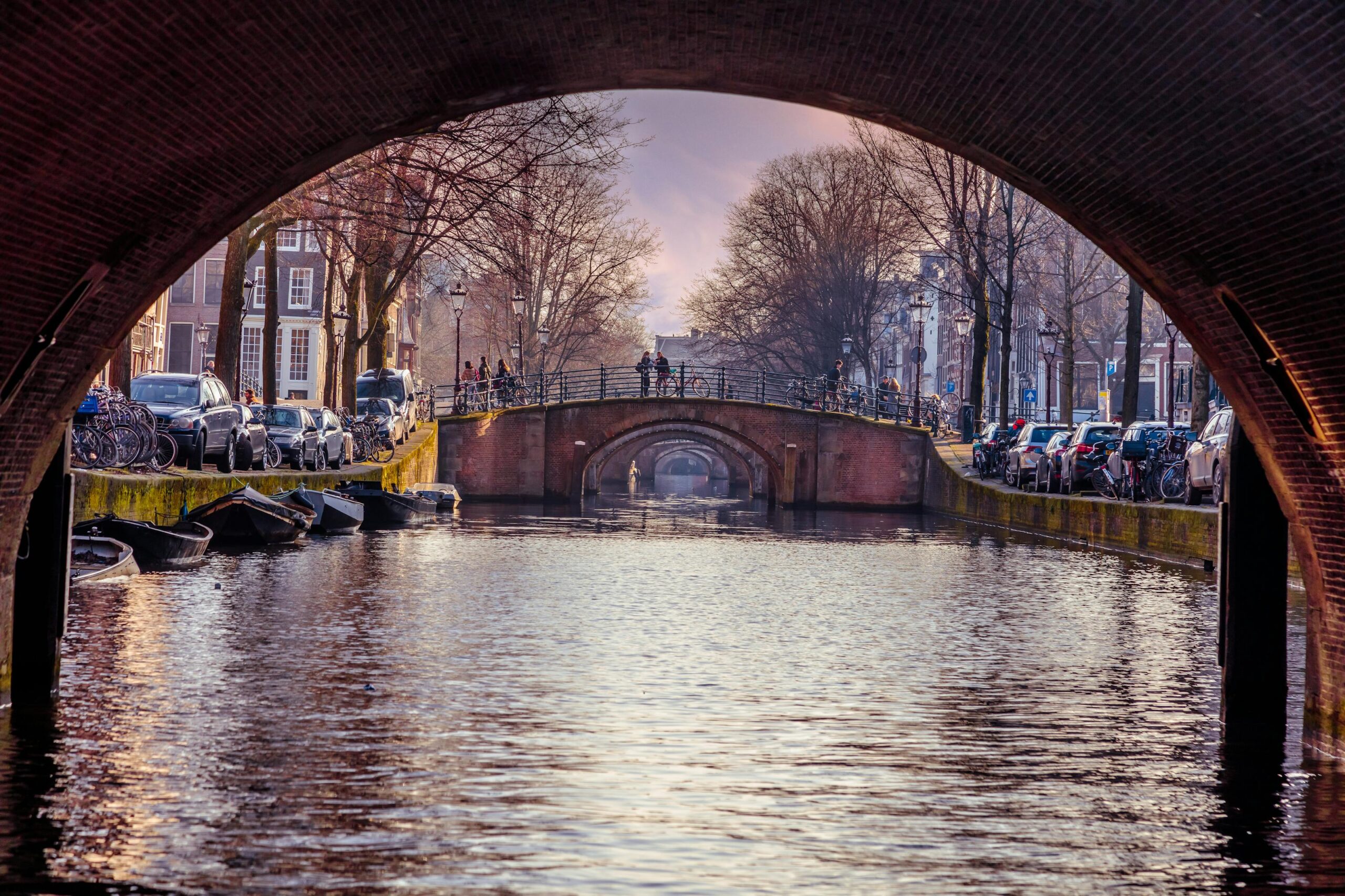 Canal de Amsterdam con barcos enmarcado por el arco de un puente, ideal para turistas jovenes