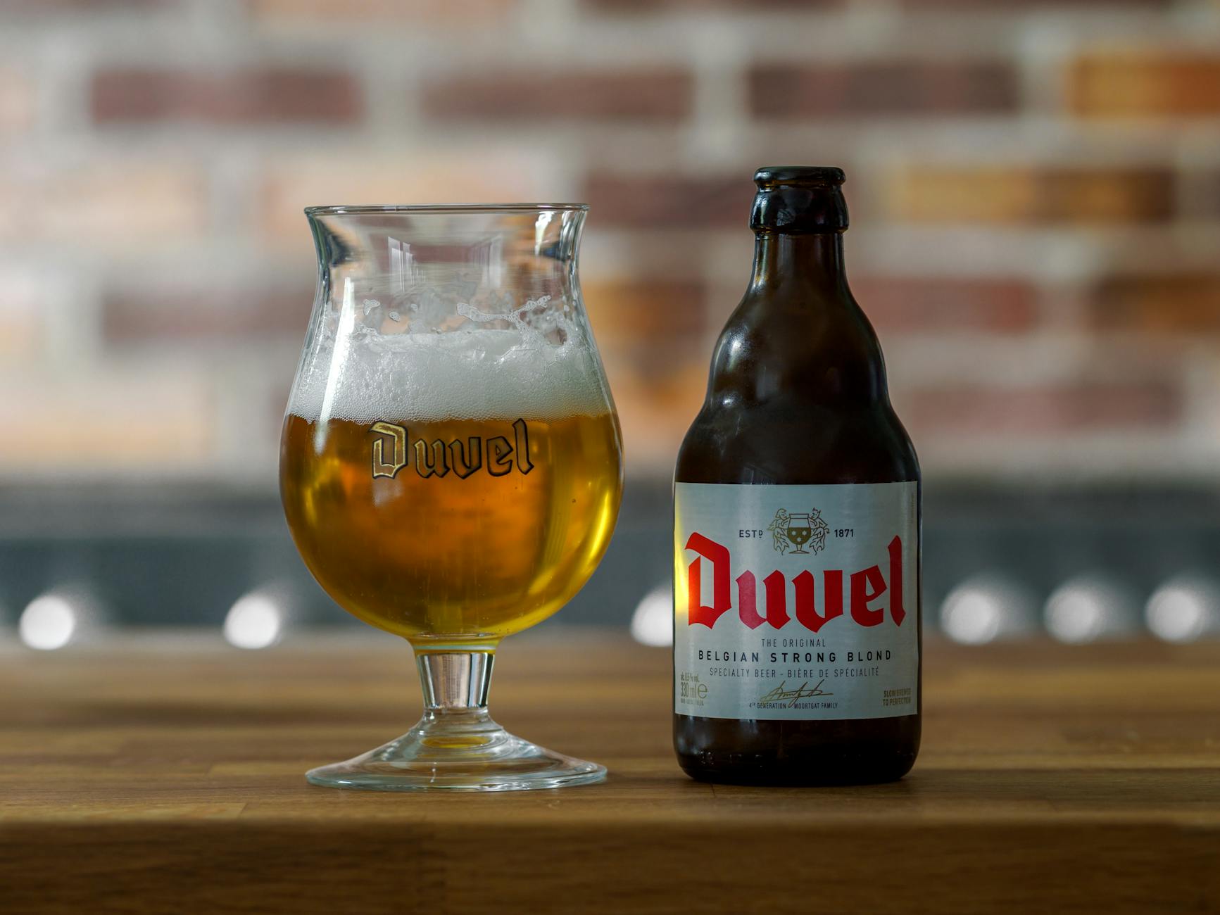 Botella y copa de cerveza belga Duvel sobre mesa de madera en bar