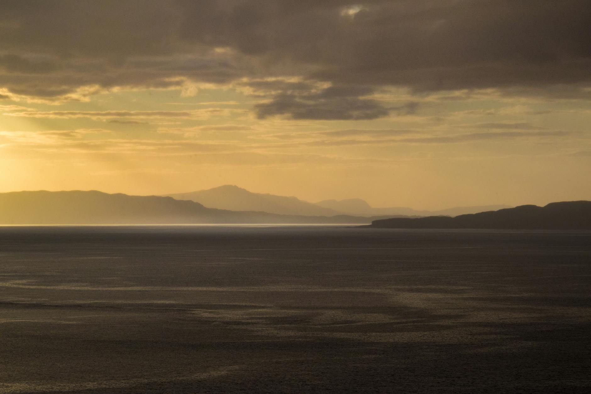 Lago en la Isla de Skye con la luz sólida del atardecer rebotando sobre el agua y las montañas al fondo