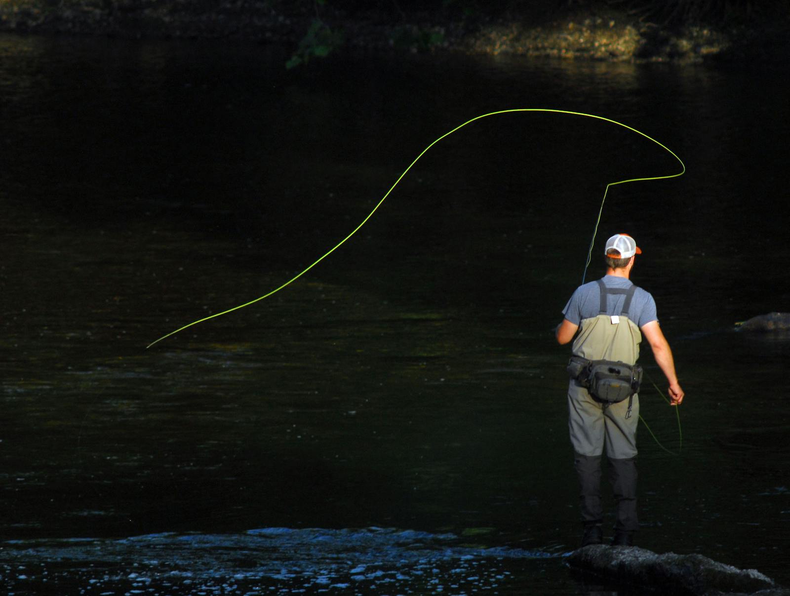 Hombre pescando con cana de mosca de pie en un rio caudaloso