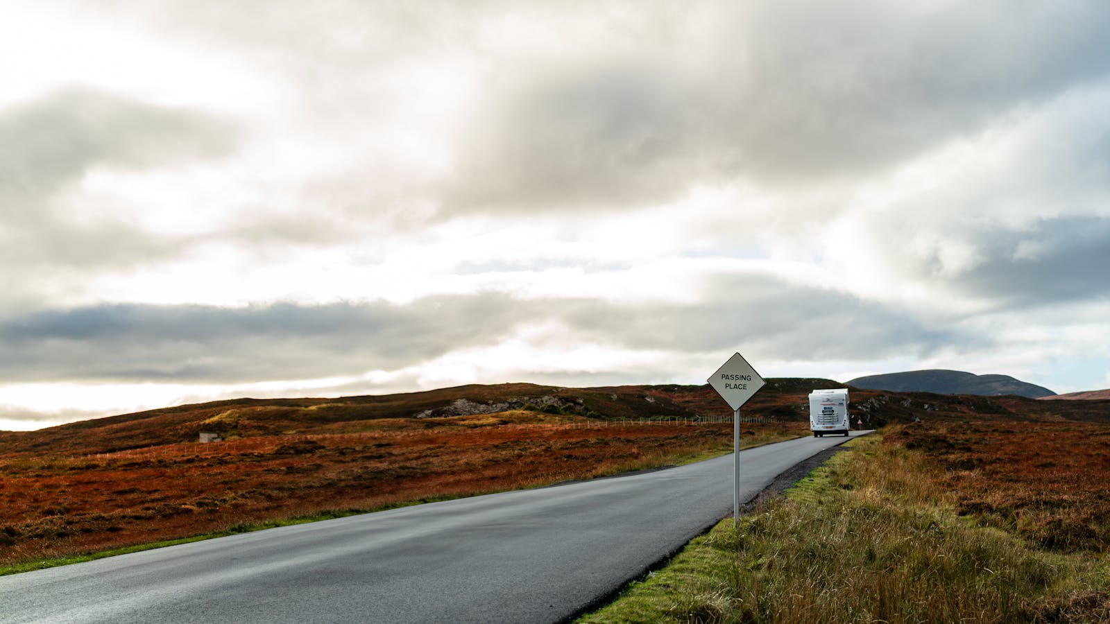 Caravana viajando por una carretera con paisaje otoñal y cielo dramático