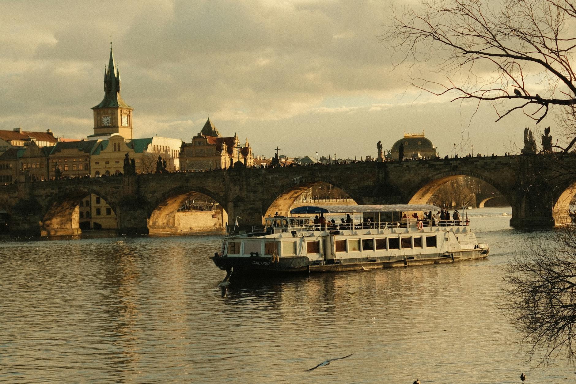 Crucero navegando bajo el Puente de Carlos en el río Vltava al atardecer en Praga