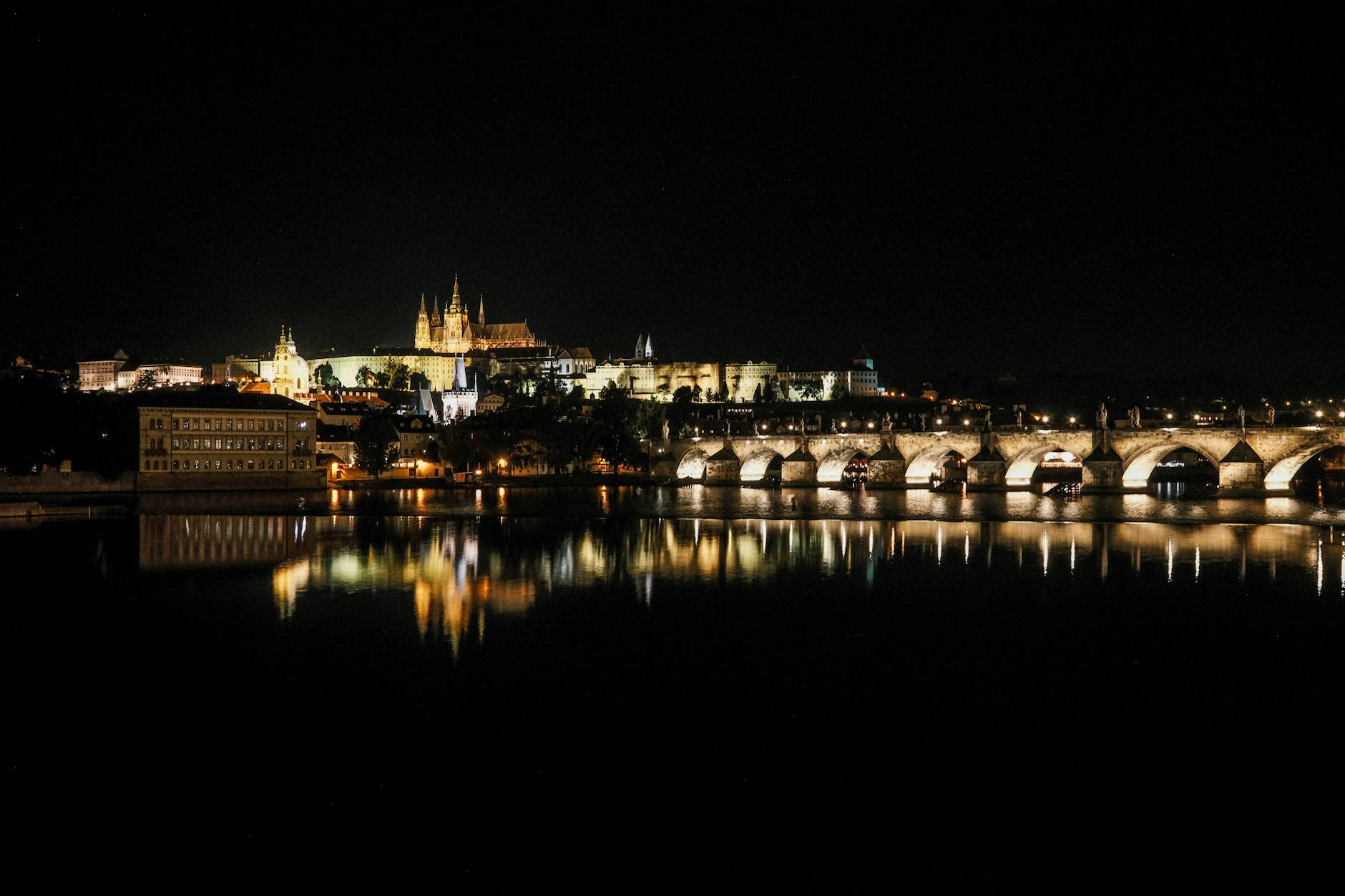 Castillo de Praga y Puente de Carlos iluminados de noche reflejados en el río Vltava