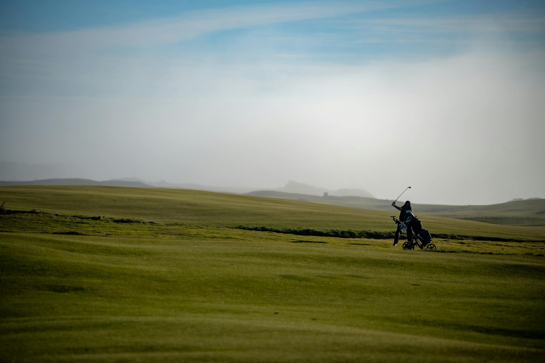 Golfista realizando un swing al amanecer en un campo amplio cubierto de neblina