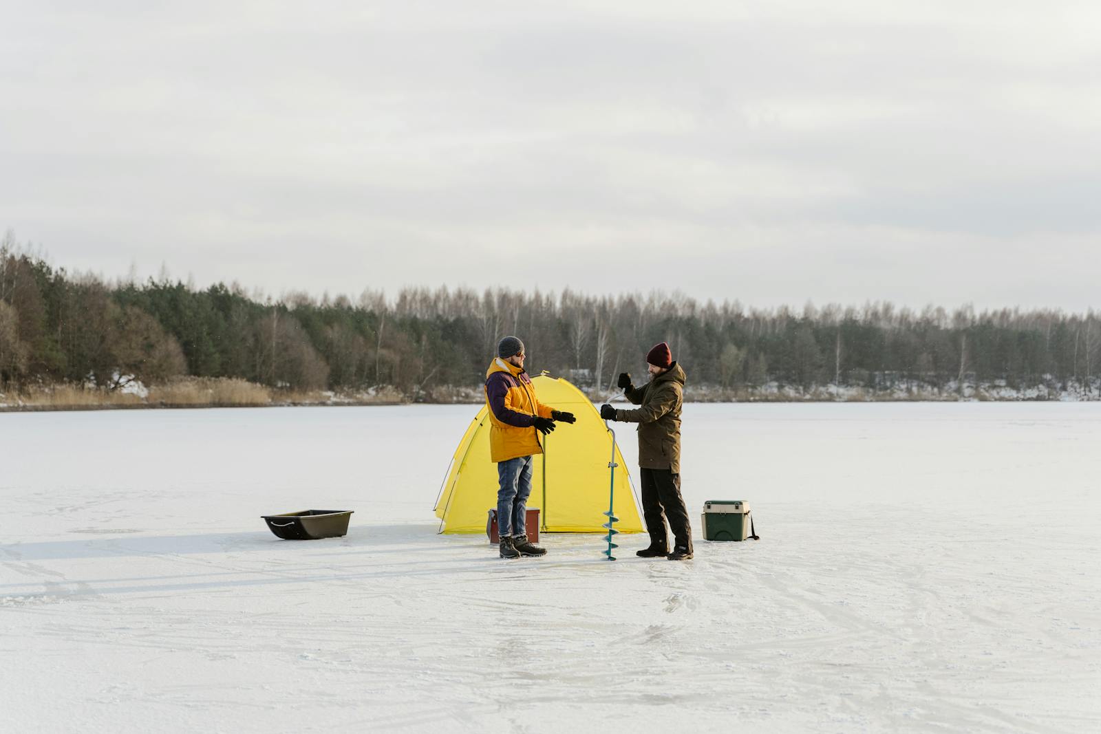 Dos pescadores en lago helado con tienda amarilla y equipo de pesca en hielo