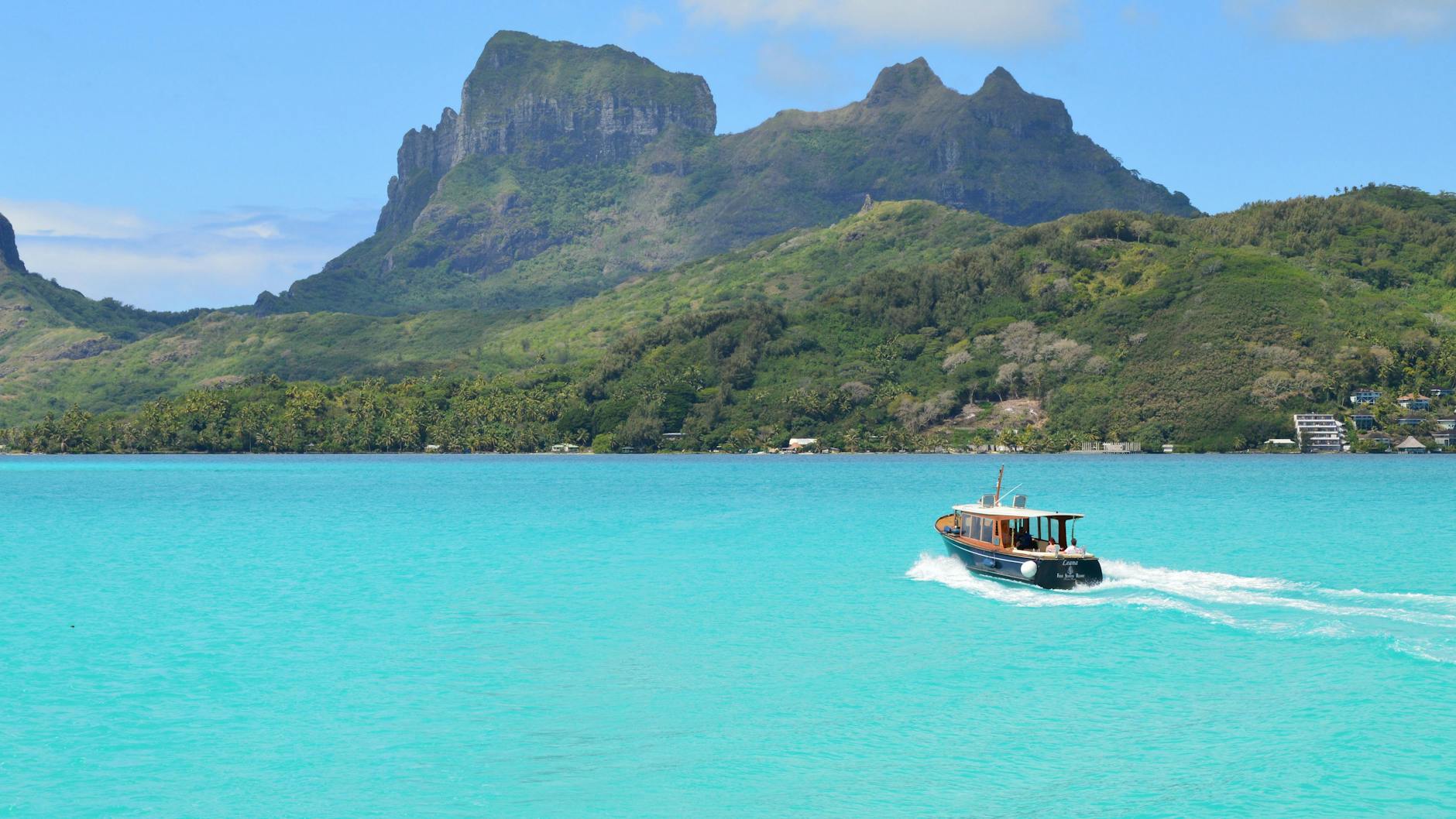 Barco navegando en aguas turquesas junto a las montañas verdes de Bora Bora