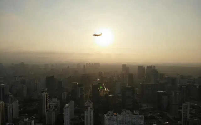 Vista aérea de ciudad con avión volando al atardecer, movilidad aérea urbana