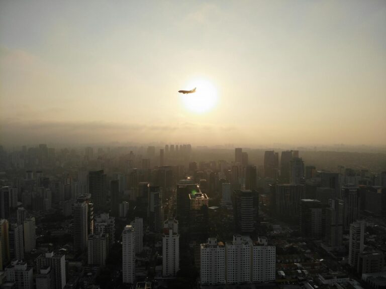 Home Elementor 4 Vista aérea de ciudad con avión volando al atardecer, movilidad aérea urbana