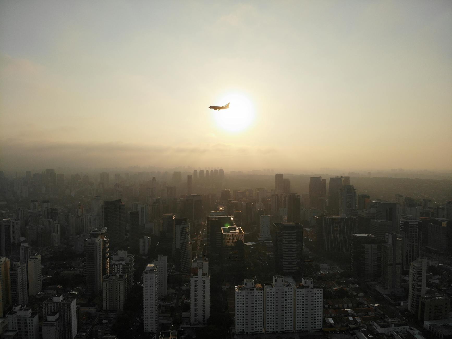 Vista aérea de ciudad con avión volando al atardecer, movilidad aérea urbana