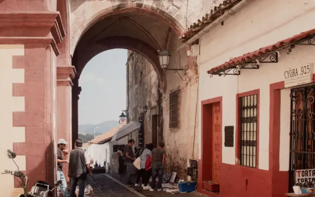 Calle empedrada de Taxco con casas blancas y la Catédral de Santa Prisca al fondo