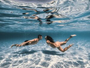 pareja buzándose juntos en el océano con equipo de buceo
