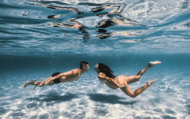 pareja buzándose juntos en el océano con equipo de buceo