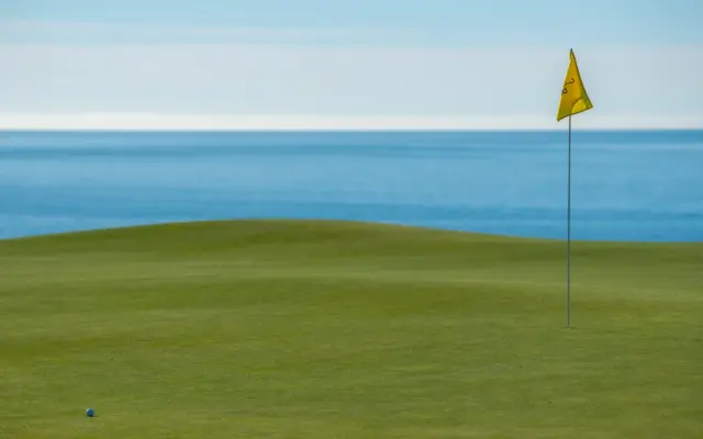 Campo de golf junto al mar con bandera y green de putt