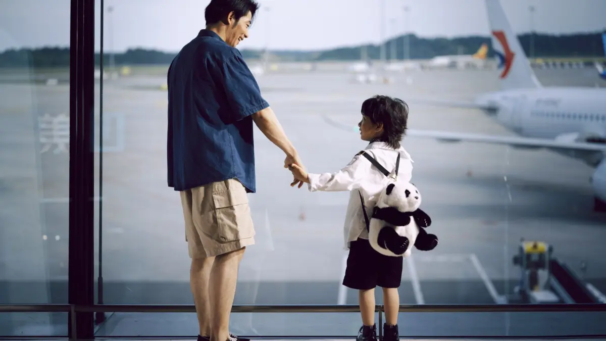 Padre e hijo de la mano mirando aviones a través de la ventana del aeropuerto