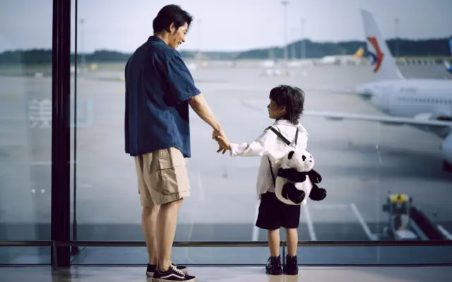 Padre e hijo de la mano mirando aviones a través de la ventana del aeropuerto