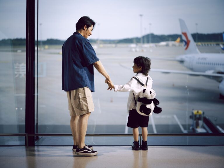 Padre e hijo de la mano mirando aviones a través de la ventana del aeropuerto