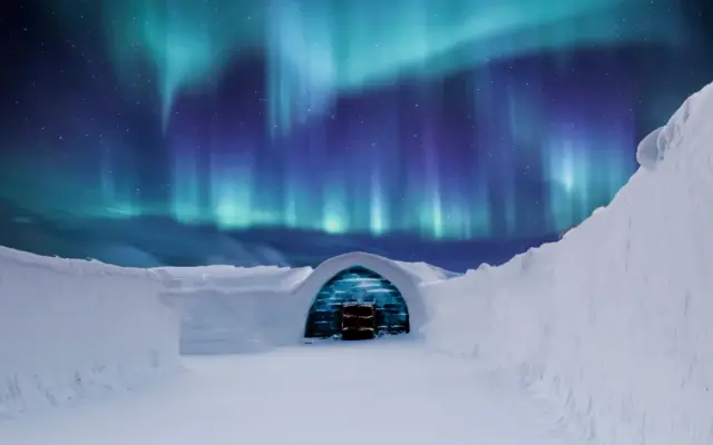 Aurora boreal sobre un iglu transparente cubierto de nieve en el ártico finlandés