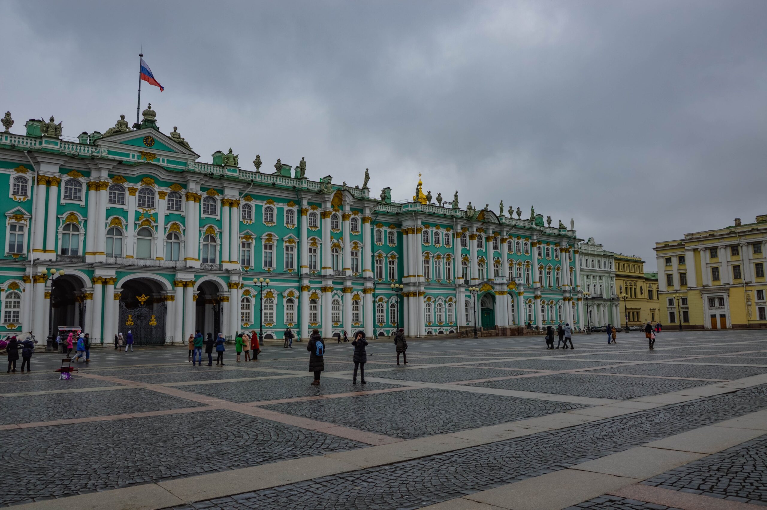 Visitantes frente al Palacio de Invierno en un día nublado en San Petersburgo