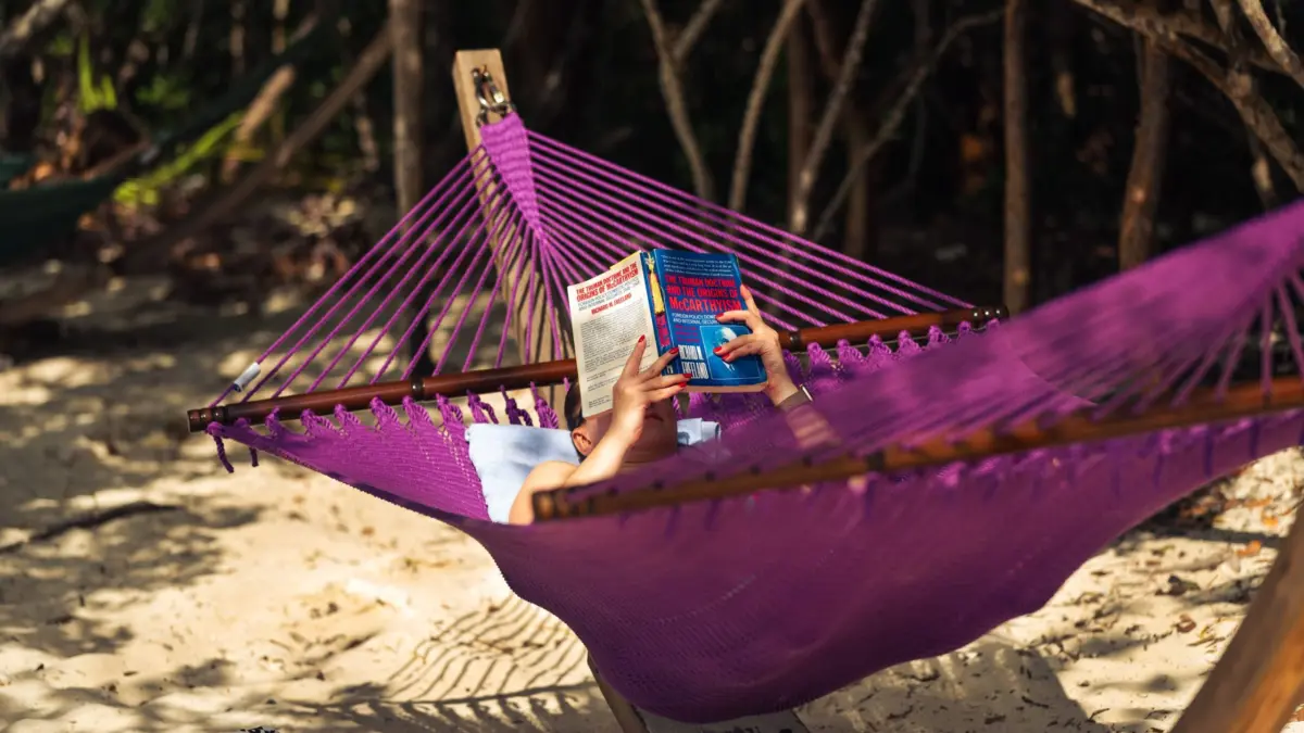 Persona leyendo en una hamaca junto a la playa, sin dispositivos electrónicos