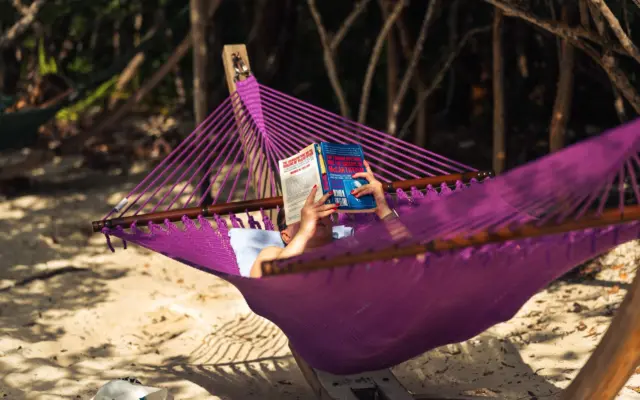 Persona leyendo en una hamaca junto a la playa, sin dispositivos electrónicos