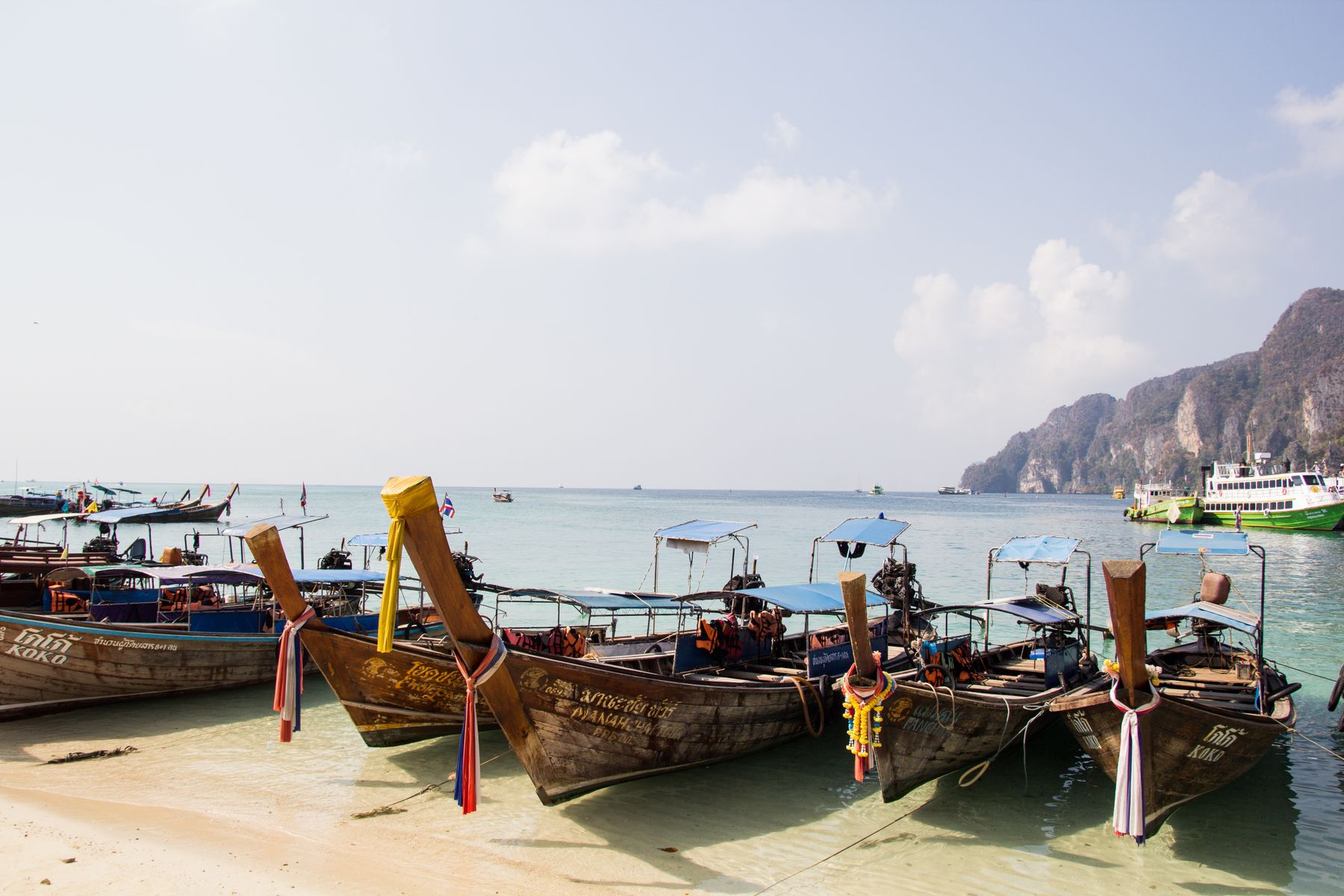 Barcas longtail amarradas en una playa de arena junto a acantilados, estilo Koh Phi Phi