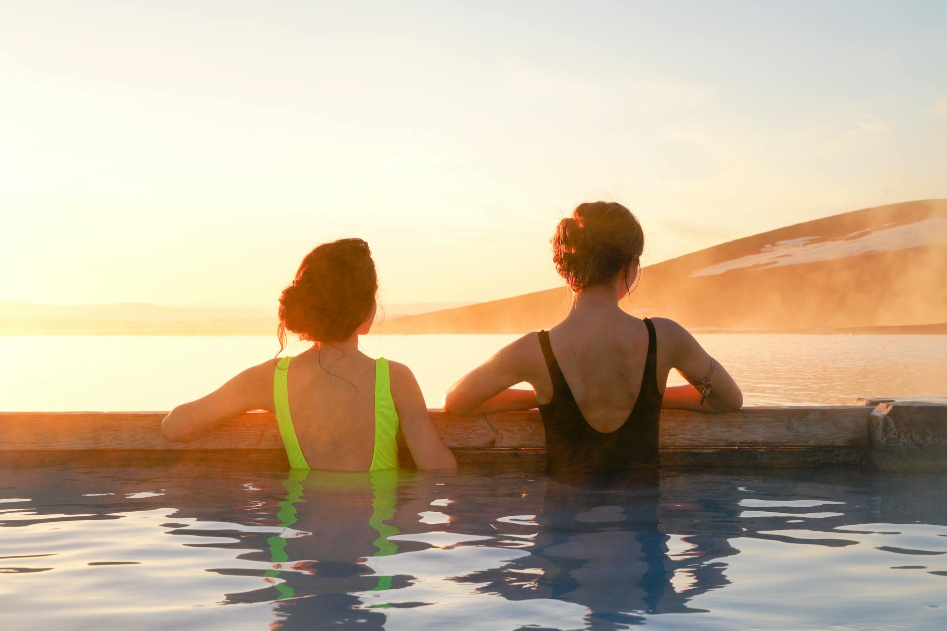 Dos mujeres disfrutan de una piscina termal natural con vistas a las montañas al amanecer