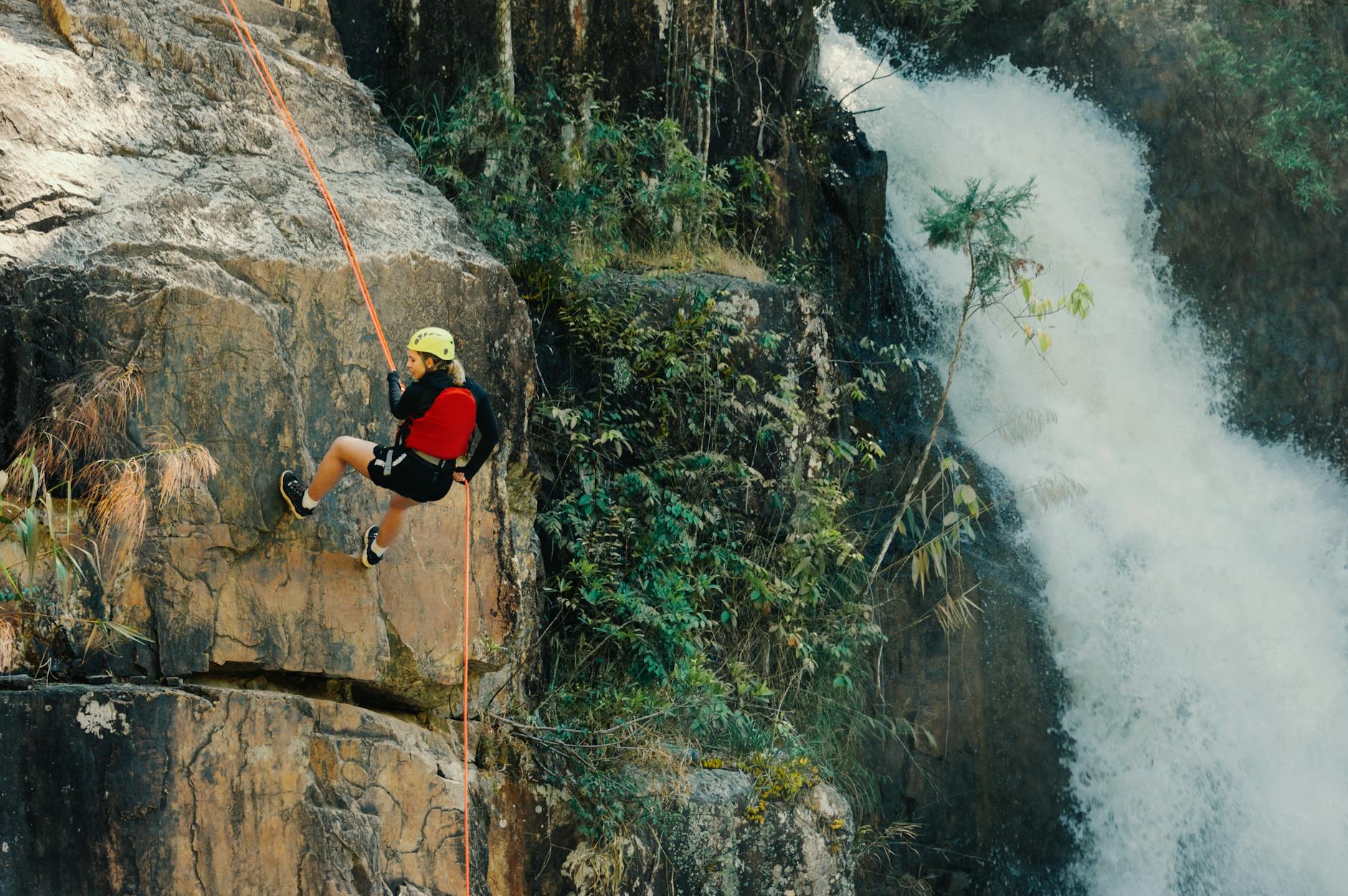 Barranquismo en España: los 6 mejores lugares y guía completa para empezar 4 Escaladora haciendo rápel junto a una cascada, técnica imprescindible en barranquismo