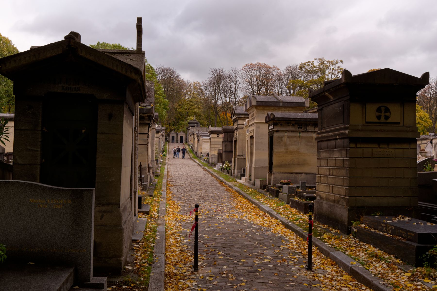 Camino de un cementerio histórico flanqueado de tumbas en un día otoñal nublado